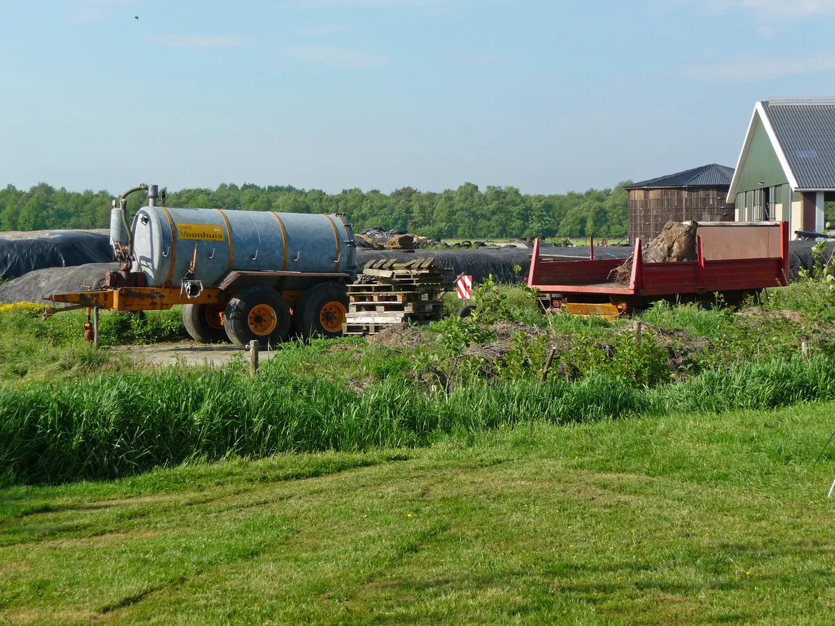 Achtererf van een Nederlandse melkveeboerderij met sleepmesttank en aanhangwagen, typisch agrarisch bedrijf