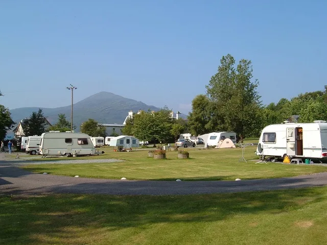 Meerdere toercaravans op een groen campingterrein met bergen op de achtergrond — allrisk caravanverzekering