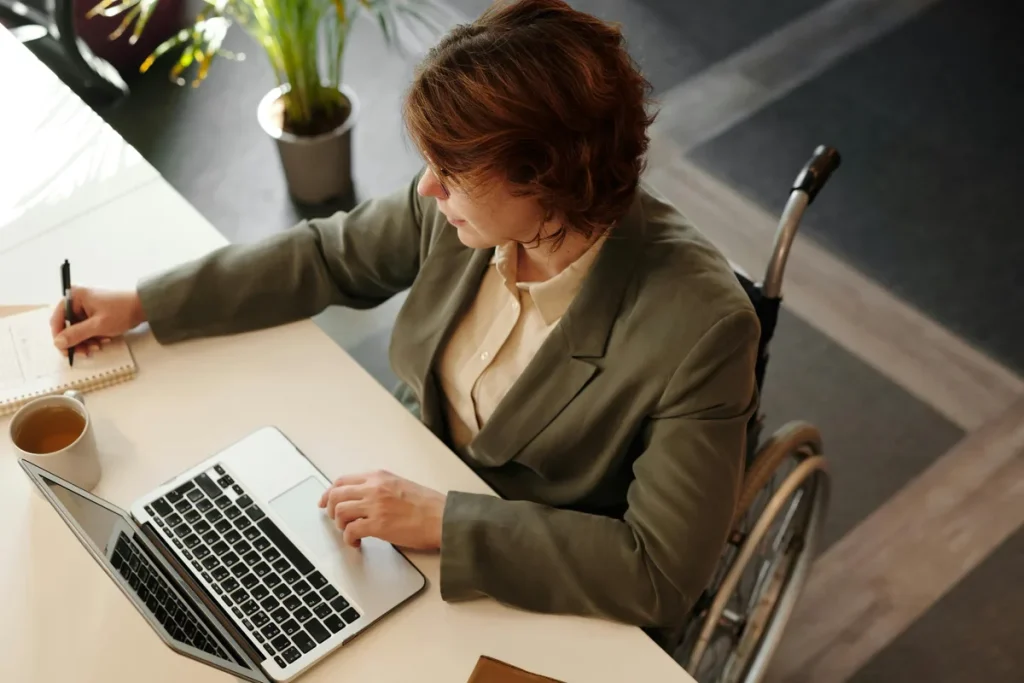 Vrouw in rolstoel werkt aan bureau met laptop, symbool voor arbeidsongeschiktheid en AOV-dekking