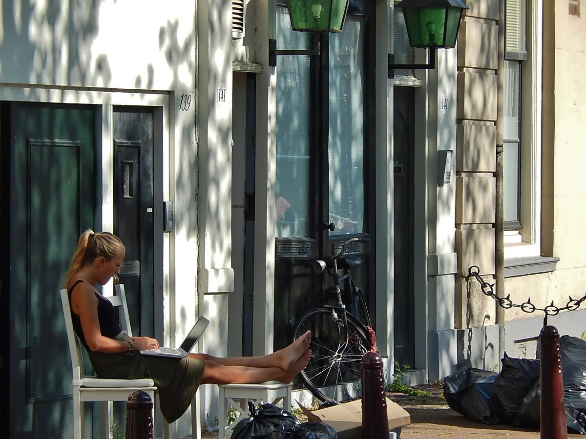Vrouw werkt op laptop buiten in Nederlandse straat - ASR verzekering online afsluiten