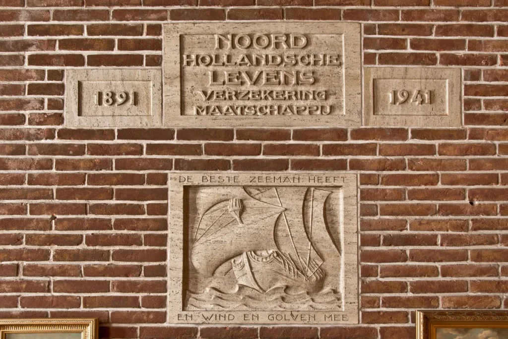 Gevelsteen Noord Hollandsche Levens Verzekering Maatschappij 1891–1941 op bakstenen wand in Nederlands kantoor