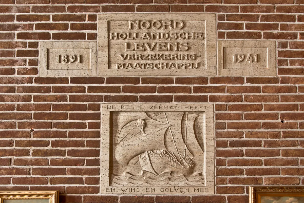Gevelsteen Noord Hollandsche Levens Verzekering Maatschappij 1891–1941 op bakstenen wand in Nederlands kantoor