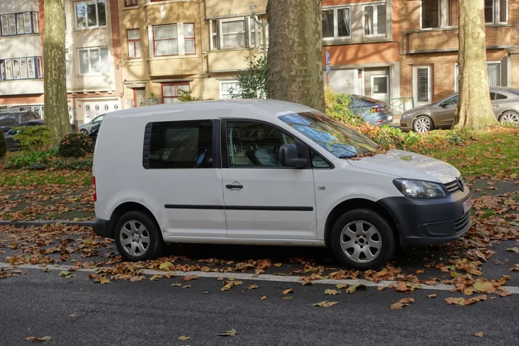 Witte VW Caddy bestelwagen geparkeerd op straat, zijkant met ramen zichtbaar