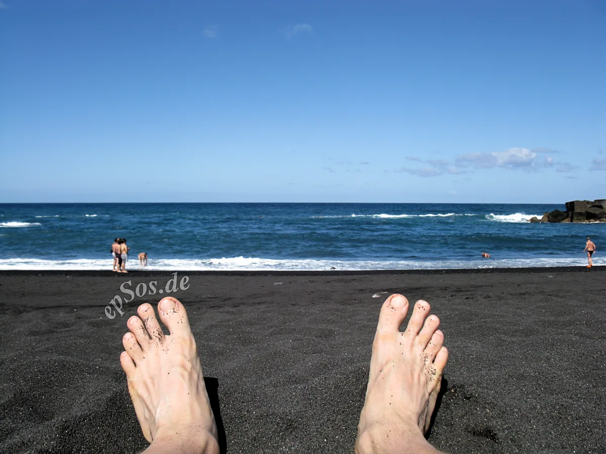 Vakantieganger ontspant op zwart zandstrand met blauw zeewater — reisverzekering voor vakantie