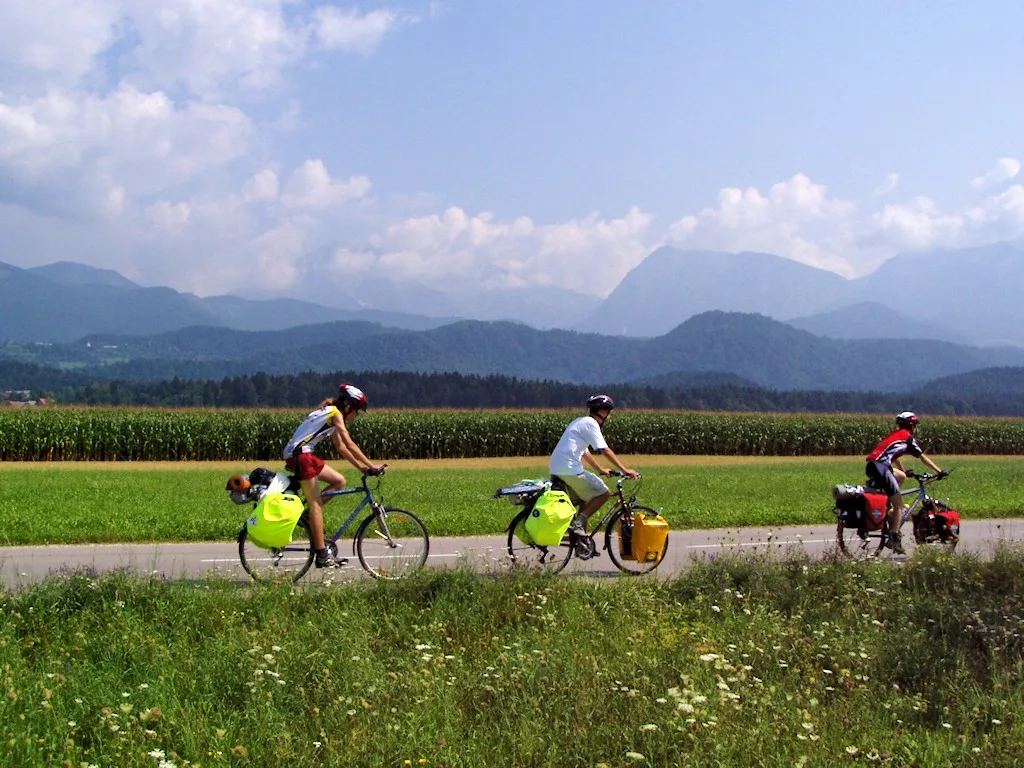 Drie fietsers op fietsvakantie met bepakte fietsen op een landweg in Slovenie met bergen op de achtergrond