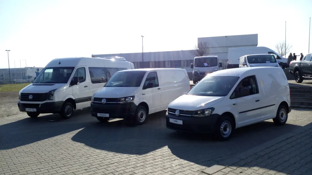 Drie Volkswagen bestelwagens (Crafter, Transporter en Caddy) op parkeerterrein — lichte vracht grijs kenteken particulier
