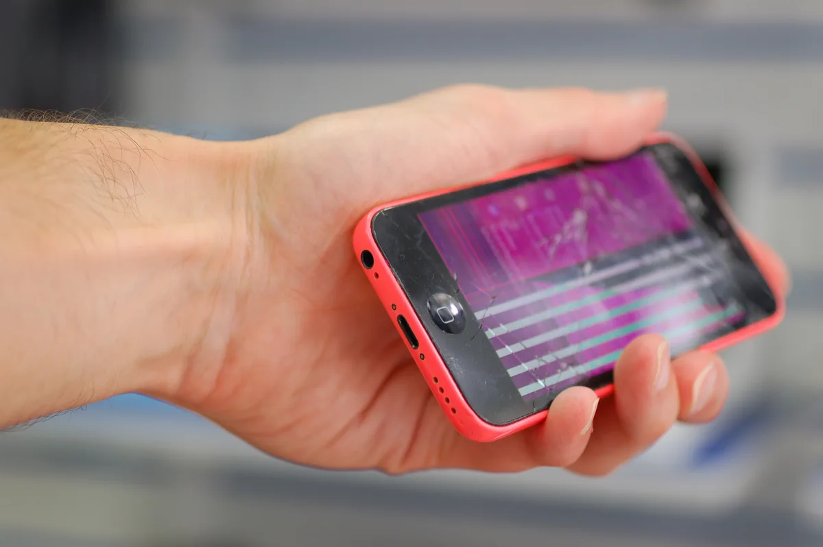 Hand houdt beschadigde iPhone met gebarsten scherm — illustratie bij telefoonverzekering en schade