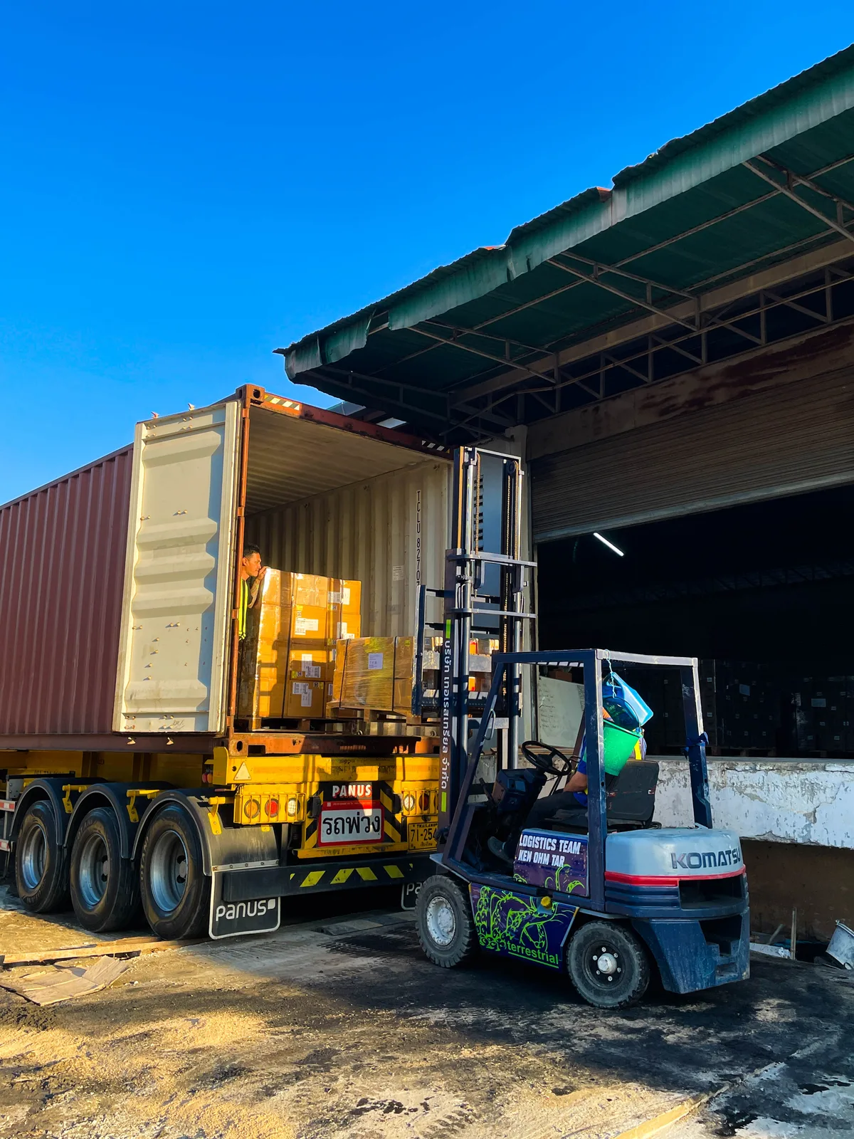 Komatsu heftruck laadt pallets in een container bij een magazijn — heftruckverzekering verplicht per WAM