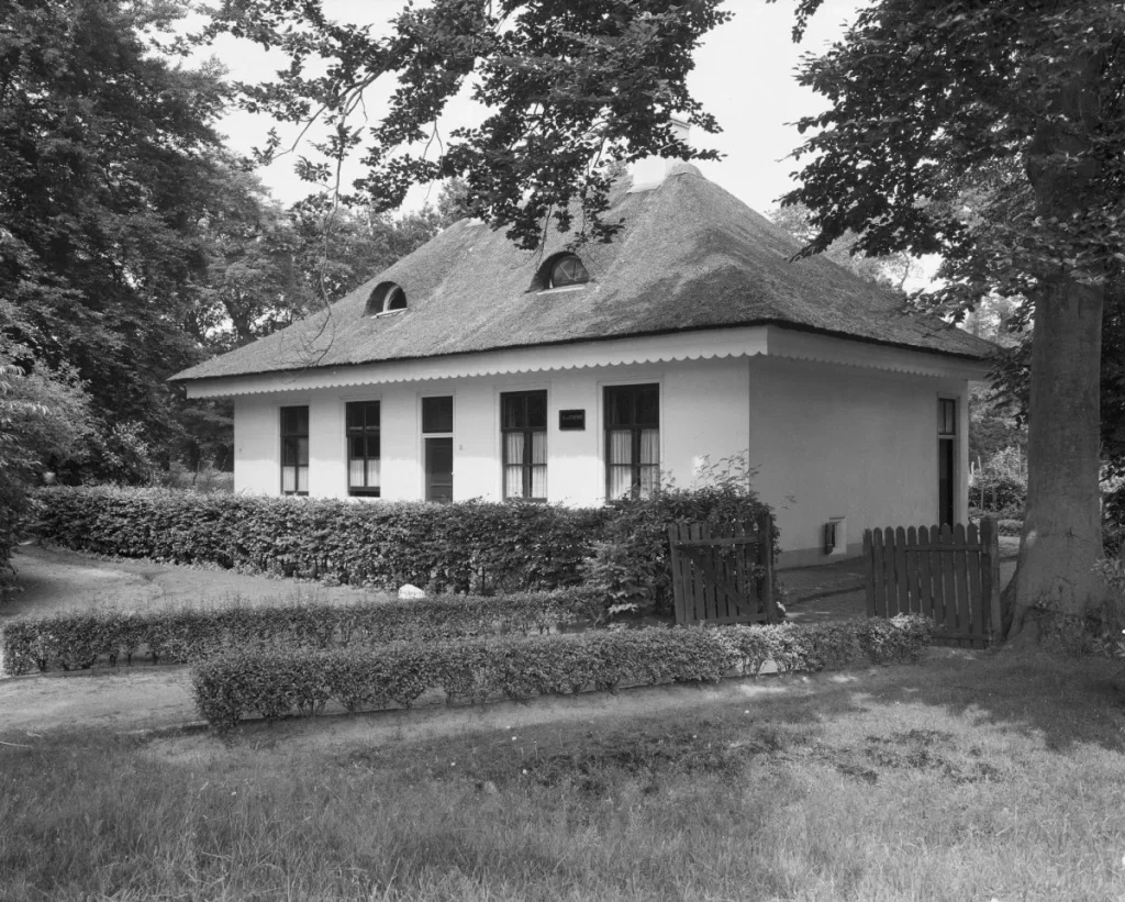 Vooraanzicht van een rietgedekte woning met dakramen in Baarn, omgeven door tuin en bomen — rijksmonument