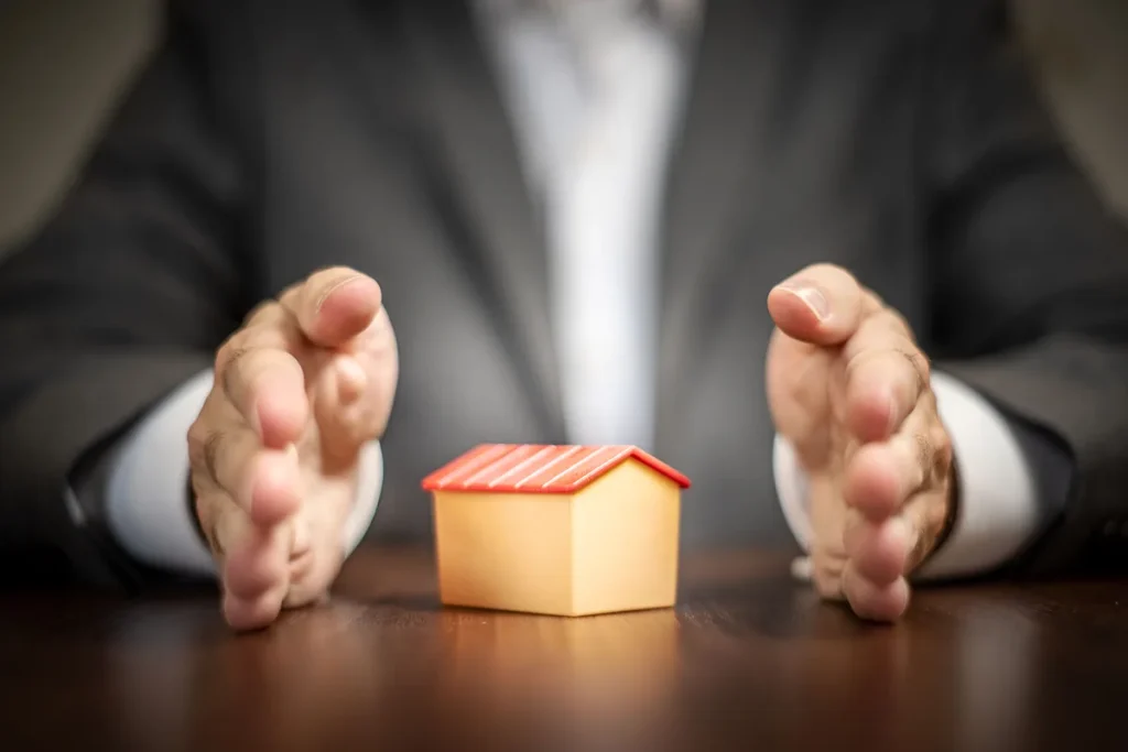 Beschermende handen om een miniatuurhuisje als symbool voor inboedel- en WA-verzekering