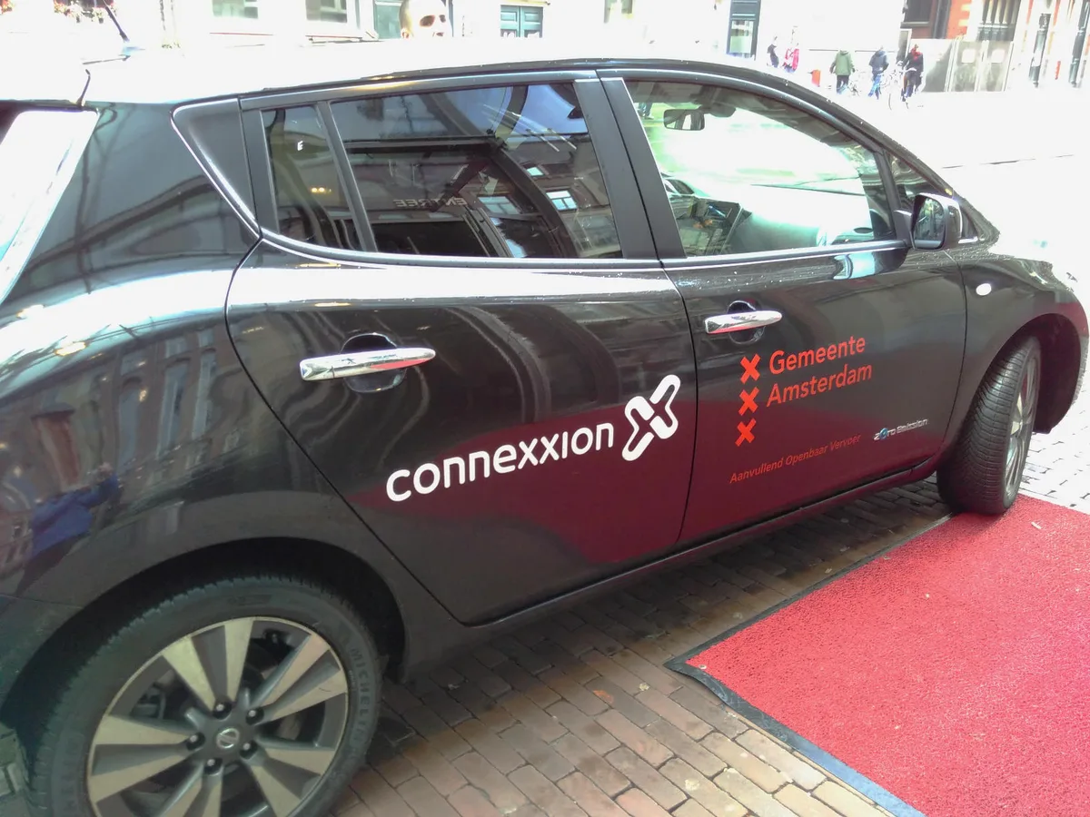 Elektrische Connexxion taxi in Amsterdam met blauwe kentekenplaat, taxiverzekering JW Verzekeringen 2026