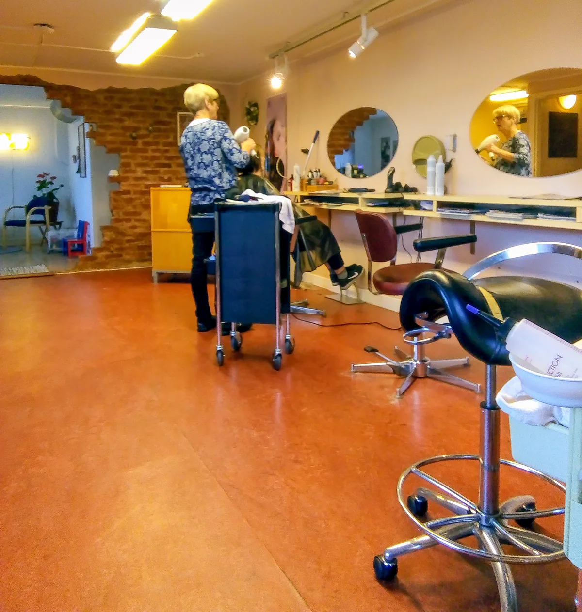 Interieur van een kapsalon met kappersstoelen, ronde spiegels en een kapper aan het werk