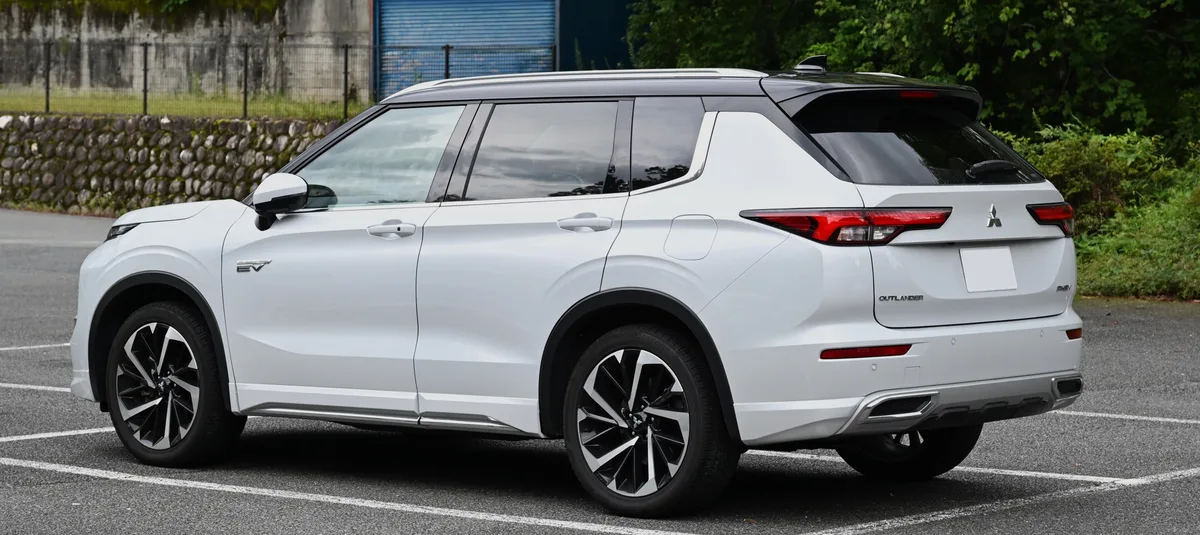 Witte Mitsubishi Outlander PHEV SUV schuin achteraanzicht op parkeerterrein, PHEV badge zichtbaar