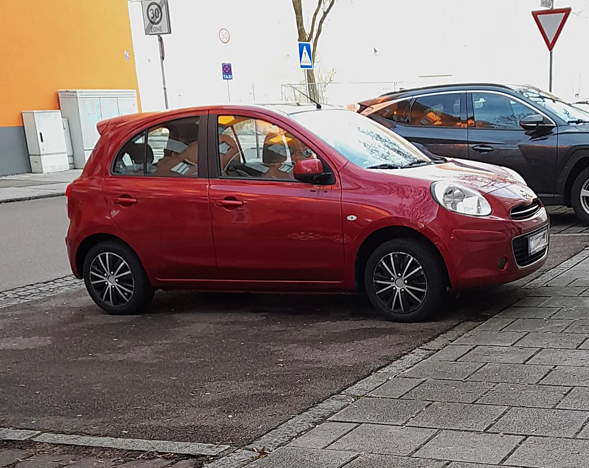 Rode Nissan Micra K13 geparkeerd op straat — compacte stadsauto populair in Nederland