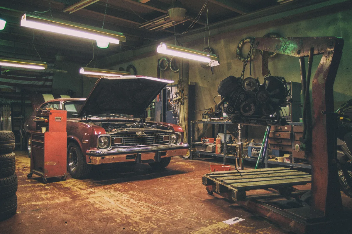 Interieur van een autogarage met een rode Amerikaanse auto en motorblok aan een kraan — autoverzekering reparatiekosten 2026