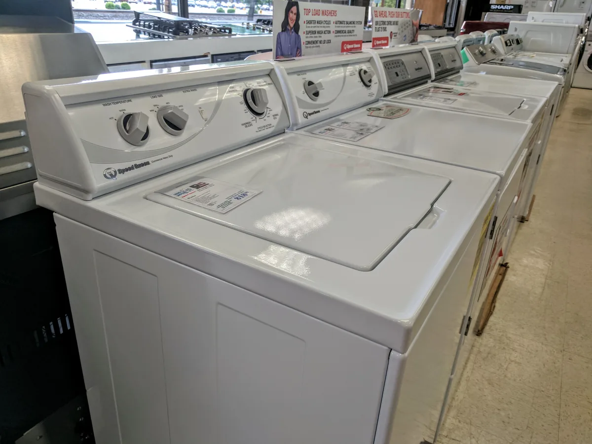 Rij witte wasmachines met prijskaartjes in een witgoedwinkel, symbool voor aankoopbescherming en garantie-uitbreiding