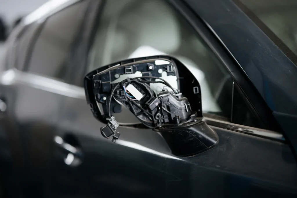 Kapotte zijspiegel van een auto met blootliggende bedrading en onderdelen in een garage