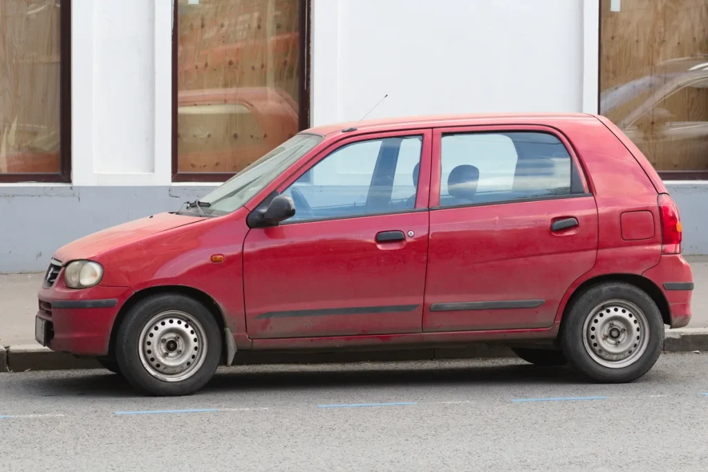 Rode Suzuki Alto hatchback geparkeerd op straat, zijaanzicht — goedkope auto voor jonge bestuurders