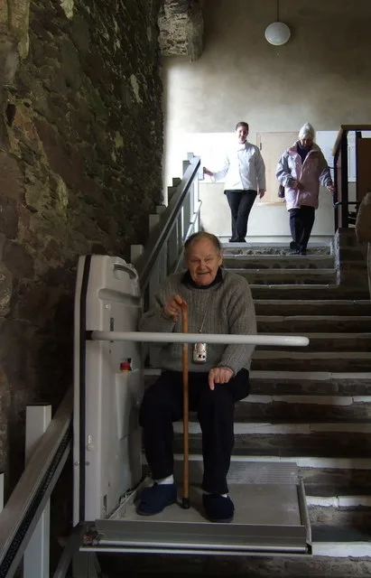 Oudere man op een traplift in een stenen trappenhuis — traplift vergoeding via Wmo
