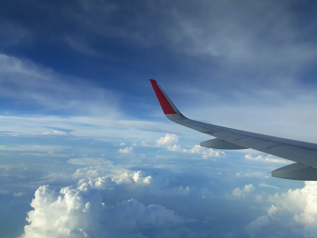 Uitzicht vanuit vliegtuigraam op vleugel en wolken tijdens vakantievlucht met reisverzekering