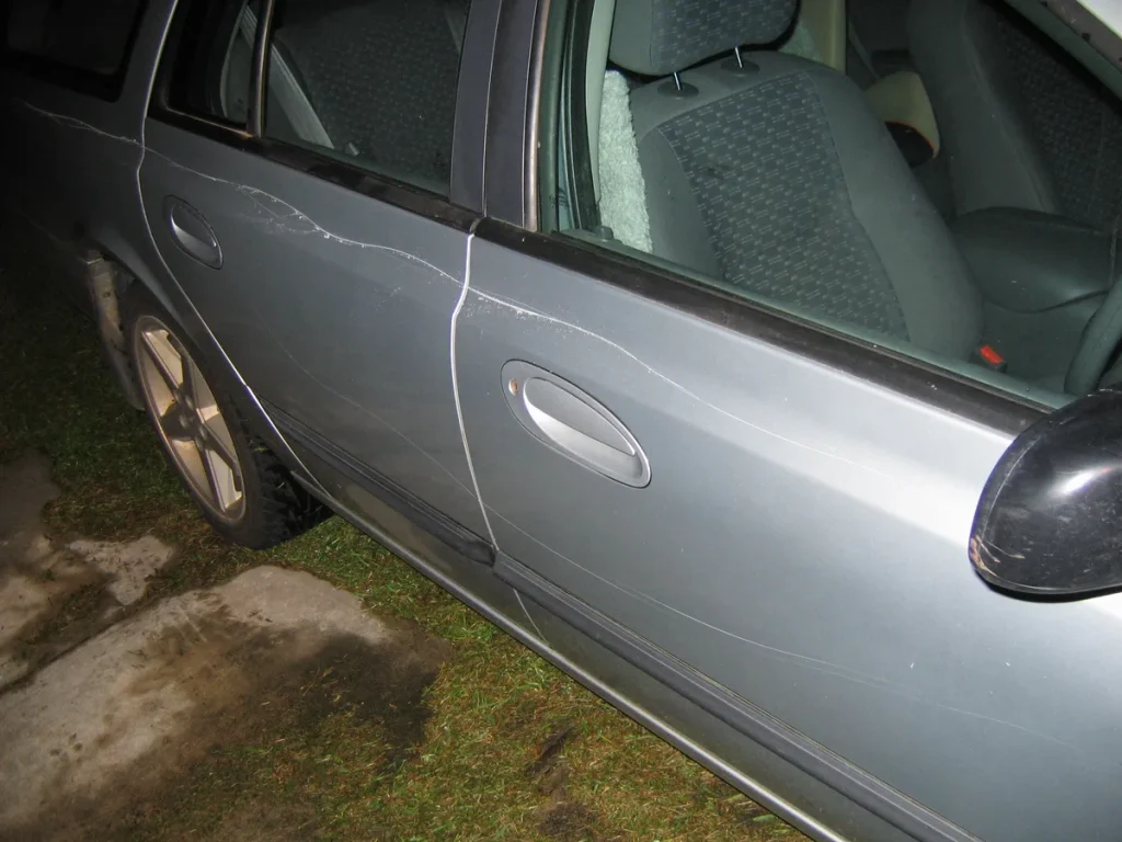 Auto met diepe krasschade door vandalisme op de portieren, zichtbaar als gevolg van opzettelijk keyen