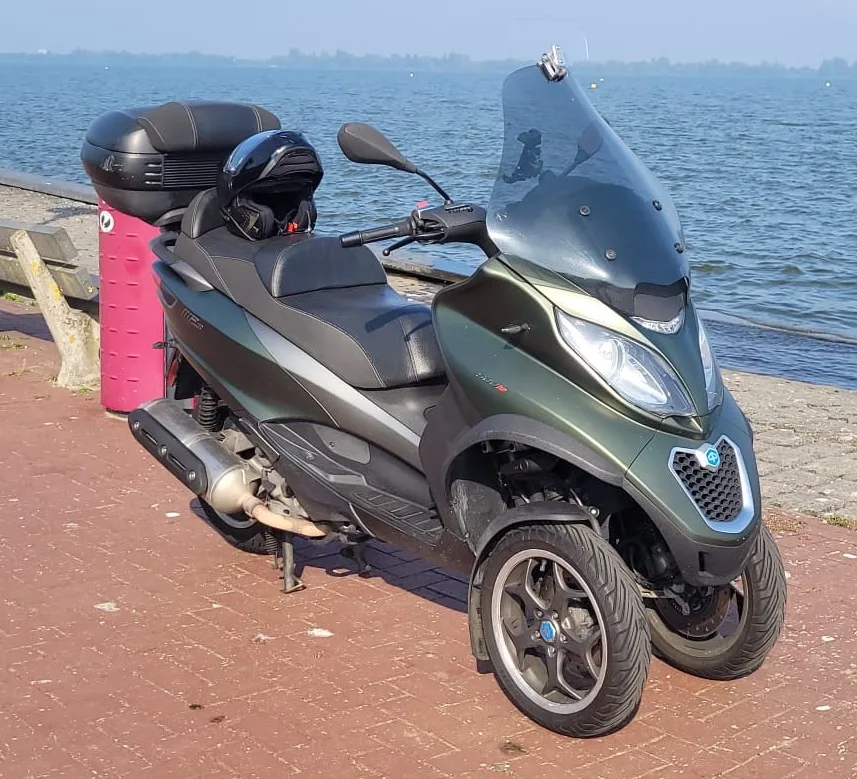 Piaggio MP3 500 LT driewieler scooter geparkeerd aan het water, twee voorwielen duidelijk zichtbaar