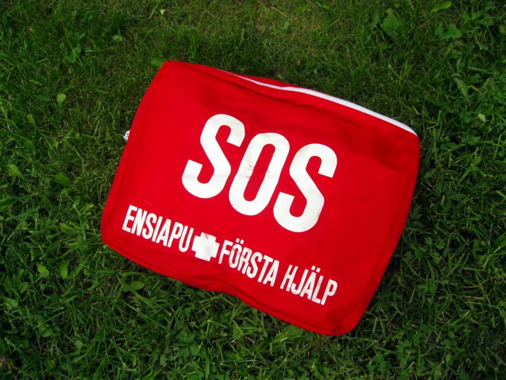 Rode EHBO-kit met SOS-opdruk op gras - symbool voor noodhulp bij een ongeluk