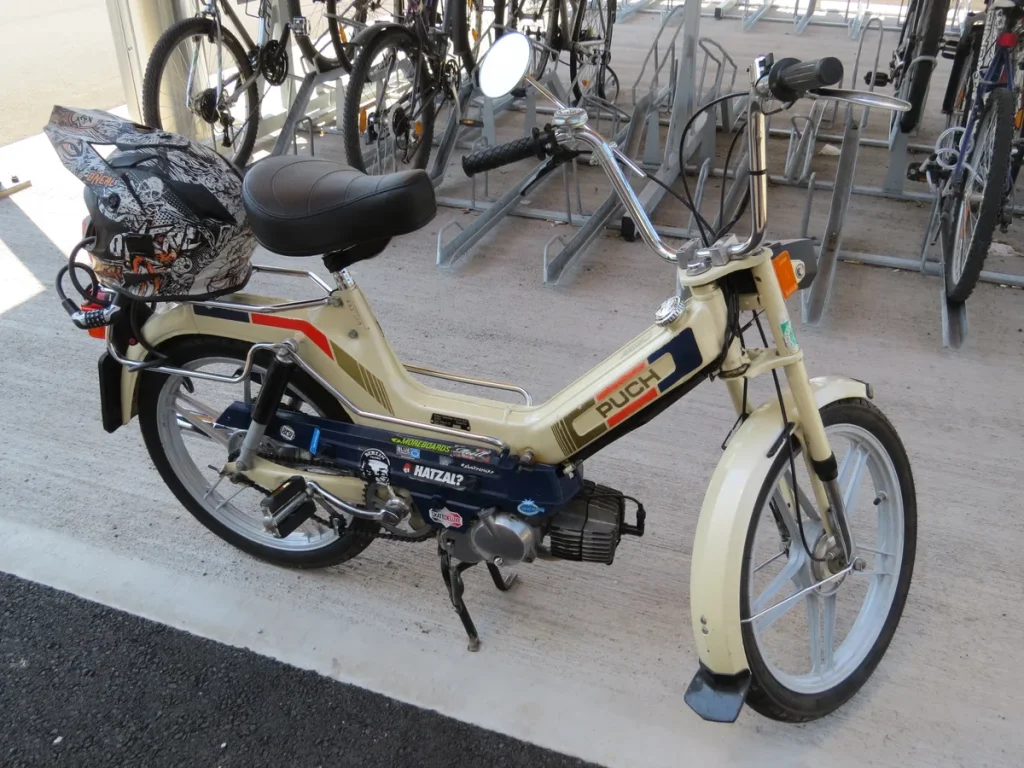 Puch Maxi S brommer klassieke oldtimer, creme met rode strepen, geparkeerd bij een fietsenstalling
