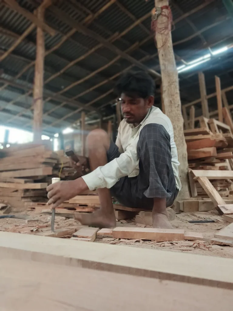 Zelfstandige timmerman aan het werk met beitel en hamer in een werkplaats vol hout