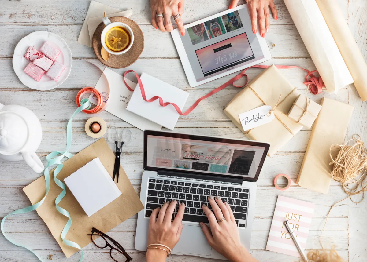 Persoon winkelt online via laptop en tablet met cadeaupakketten eromheen, webshop verzekering